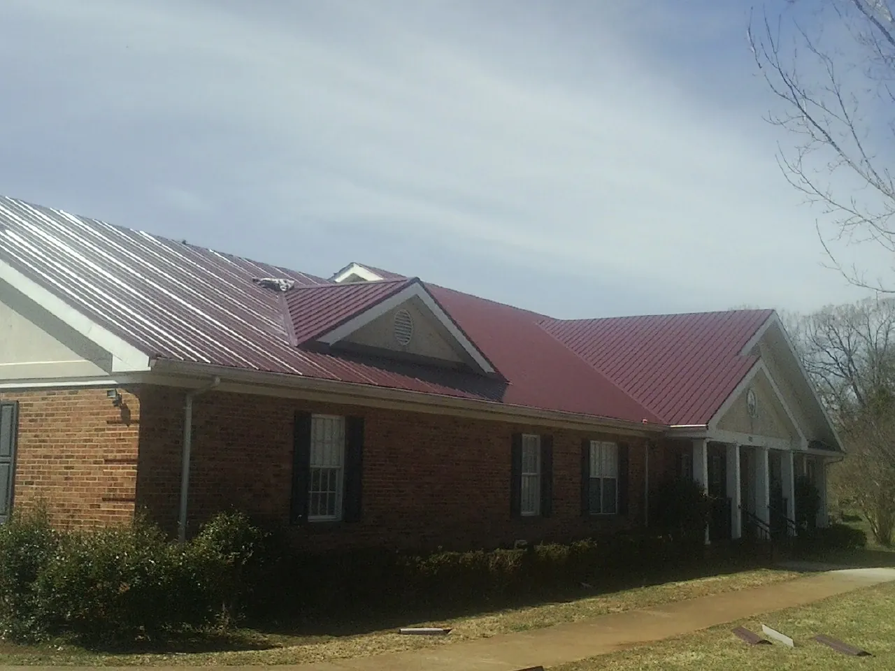 Red metal roof with gabled entries on a long brick building, from a Hail Damage Roof Repair job in Tariffville