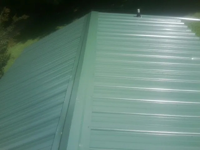 New green metal panels meeting at the ridge of a roof — Flat Roof Repair work by our crew in Tariffville