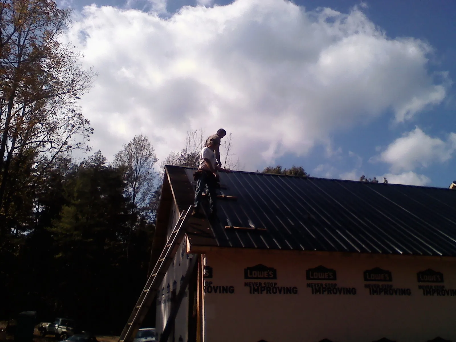 Roofer fastening dark metal panels high against a cloudy sky, from a Roof Inspection job in Tariffville