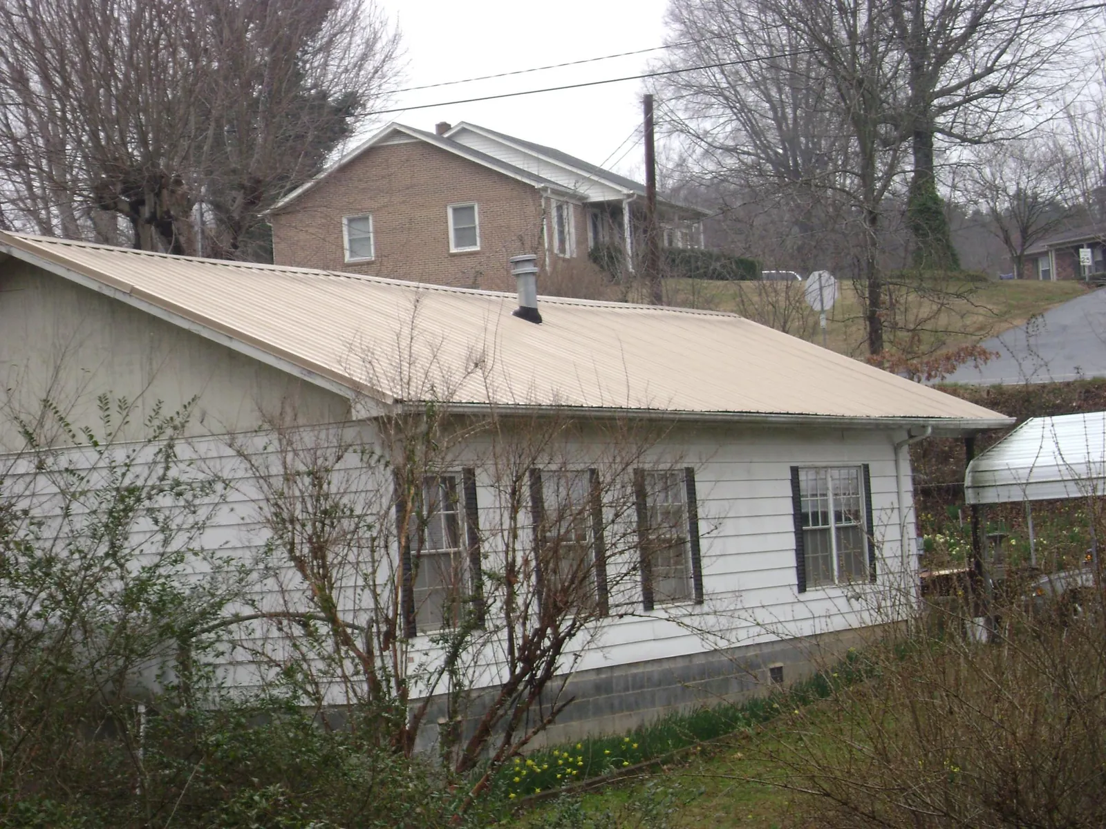 Tan metal roof on a white sided house set into a hillside — Commercial Roofing by Roofing Brothers in Tariffville