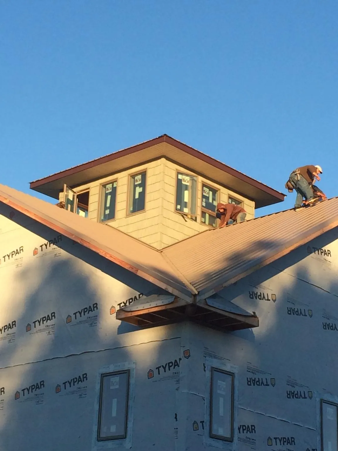 Roofers working around a rooftop cupola on a new metal roof at sunset — Roof Waterproofing in Tariffville by Roofing Brothers